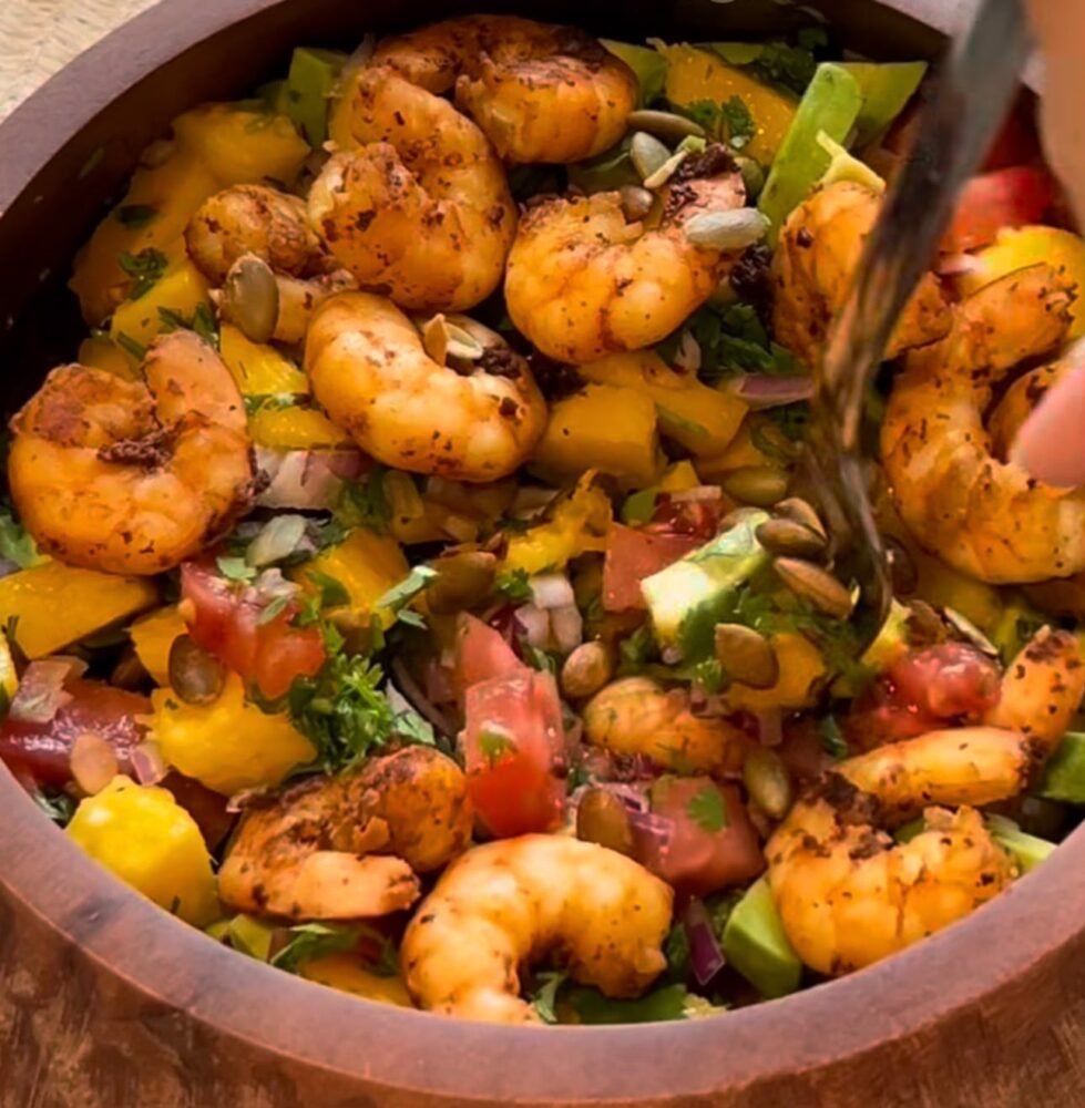 Tropical shrimp salad with mango, avocado, cucumber, greens, and lime dressing in a bowl.